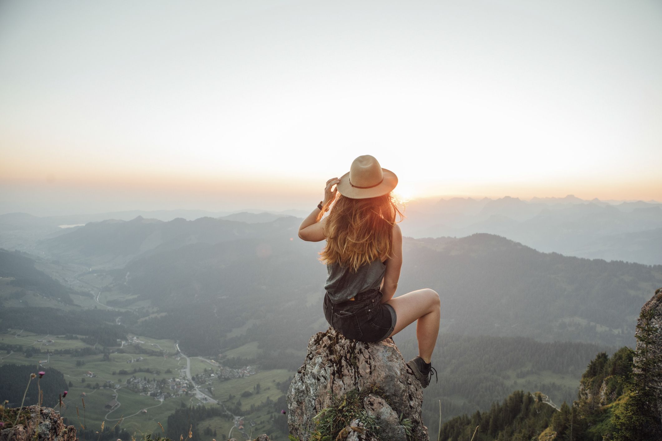 Una mujer joven sentada sobre una roca en las montañas mira con confianza el paisaje.