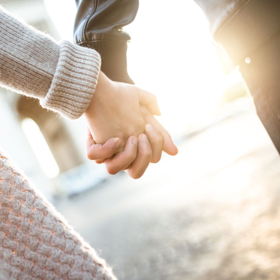 Una pareja joven camina de la mano bajo la luz del sol y comparte valores comunes para una relación duradera.