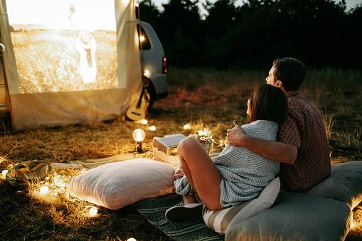 Joven pareja sentada delante de un coche durante una sesión de cine al aire libre, ilustrando una relación seria, la comunicación y los primeros momentos de una relación duradera.