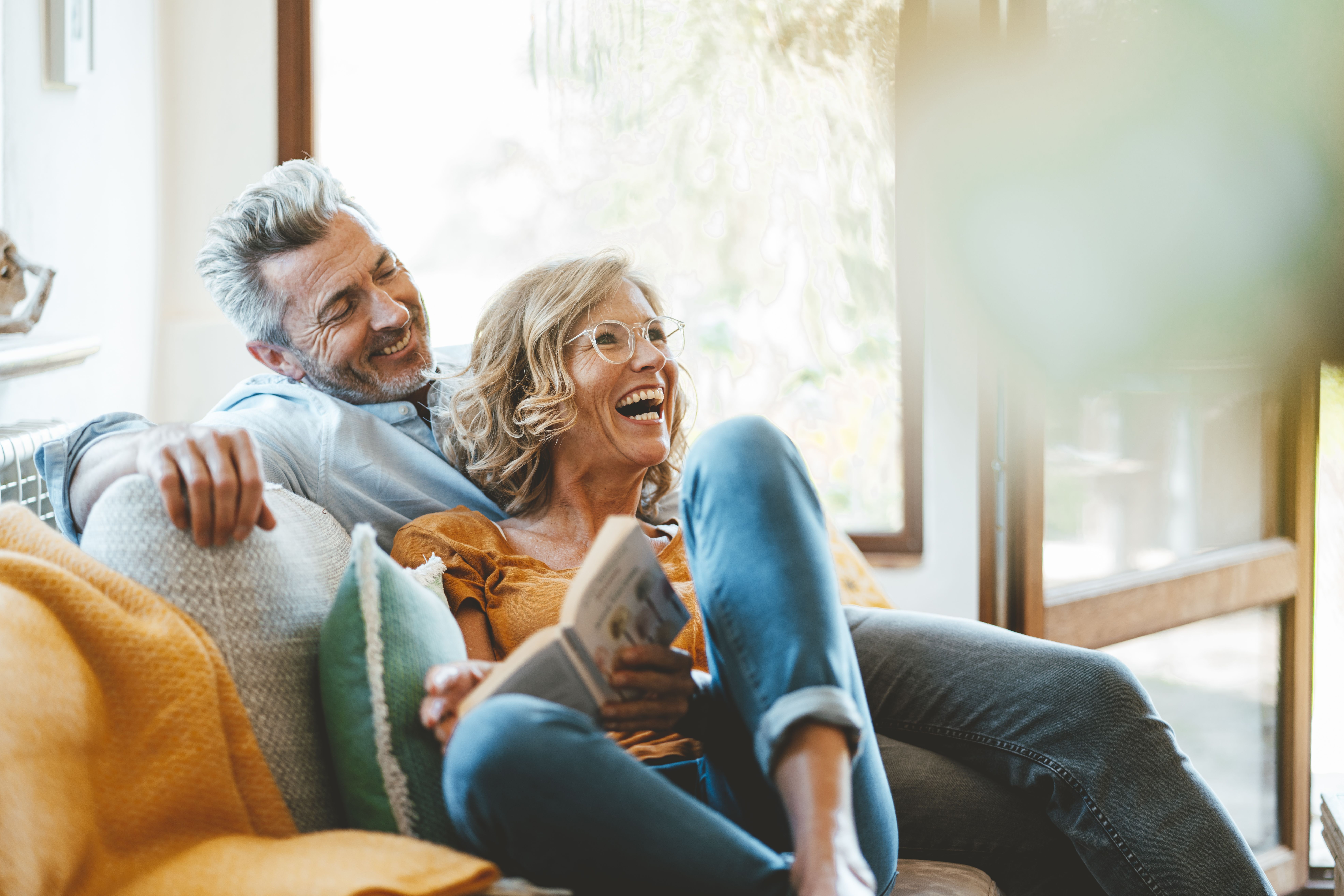 Pareja de unos cuarenta años sonriendo en un sofá en casa, compartiendo un momento de complicidad, ilustrando una relación duradera, valores compartidos y una relación seria exitosa.