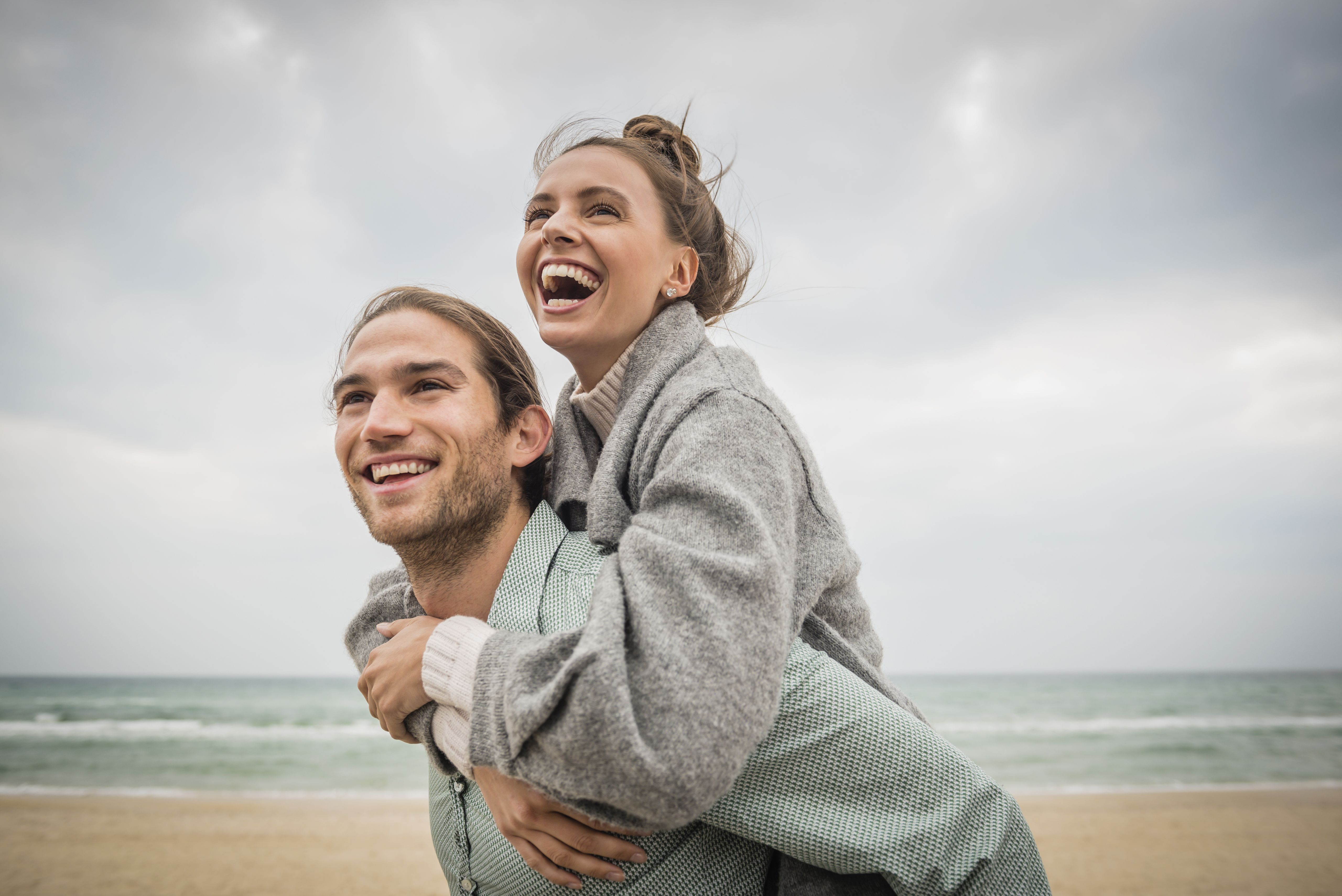 Joven pareja feliz en una playa soleada, él llevando a ella a la espalda, ilustrando una relación seria, una relación duradera y momentos de complicidad